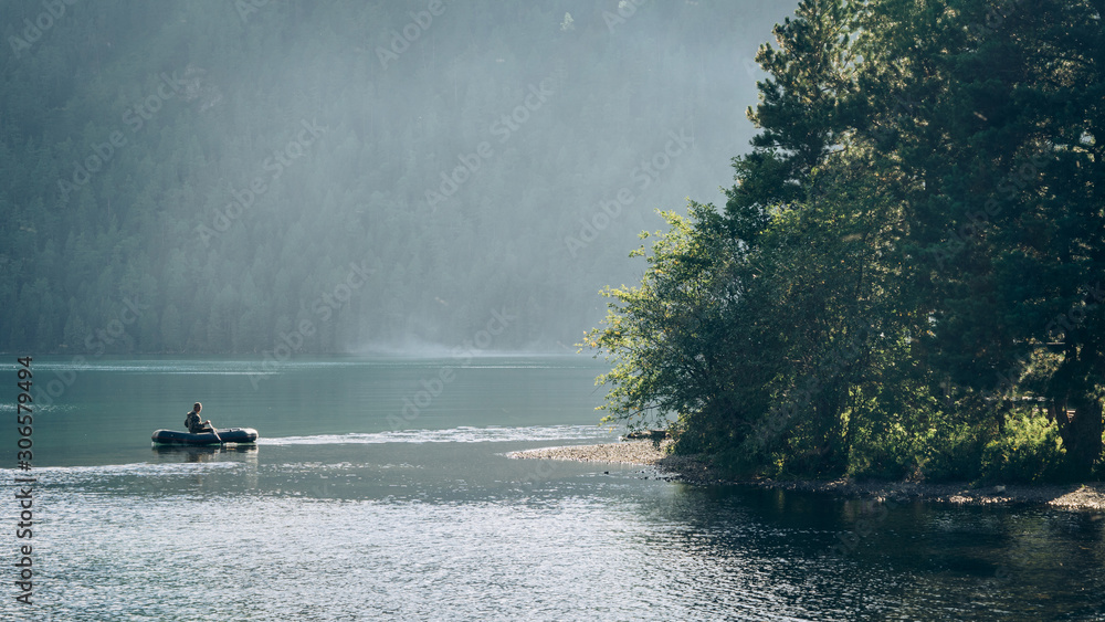 Fototapeta premium A boat with a fisherman sailing in the backlight against the background of the forest. Fishing in Siberia and Altai. Katunsky nature reserve.