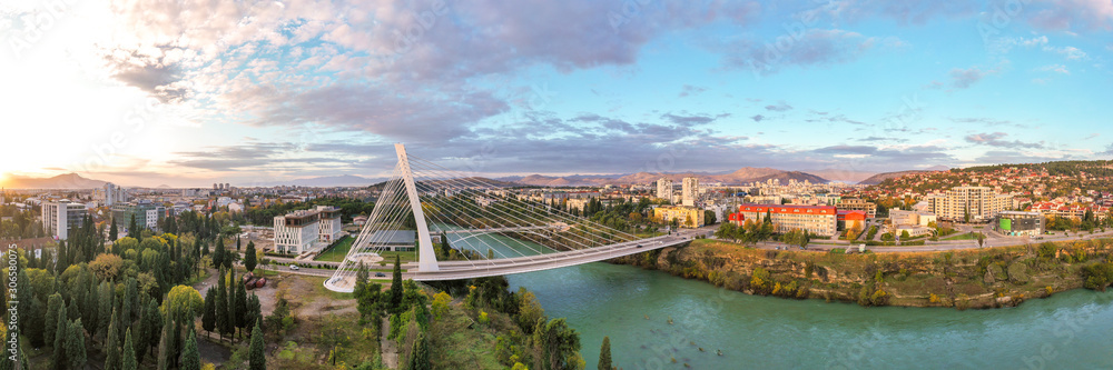 Podgorica, Montenegro: aerial view of Millennium bridge and Moraca river in the morning, at sunrise, under beautiful sky. Cable stayed bridge with green area in the foreground. 180 degree panorama.