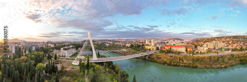 Podgorica, Montenegro: aerial view of Millennium bridge and Moraca river in the morning, at sunrise, under beautiful sky. Cable stayed bridge with green area in the foreground. 180 degree panorama.