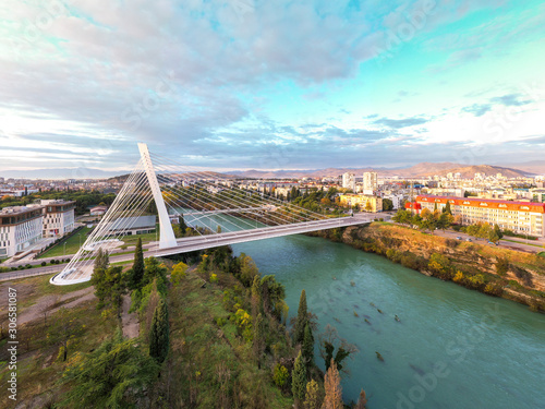 Podgorica, Montenegro: aerial view of the city featuring Millennium bridge and Moraca river in the morning, at sunrise, under beautiful sky. Cable stayed bridge with green area in the foreground.