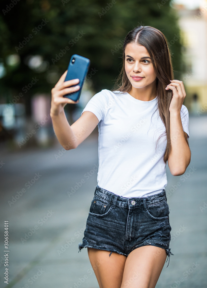 Happy woman greeting during a video call with a smart phone on the street