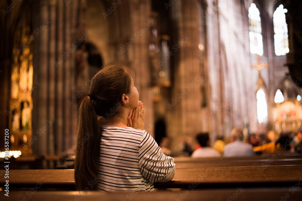 Young girl praying in church standing on her knees - obrazy, fototapety, plakaty 