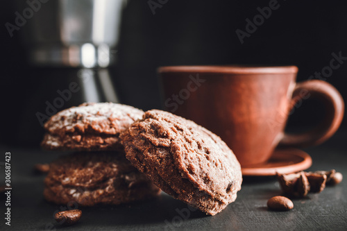 Chocolate cookies with powdered sugar and brown cup with hot drink  coffee or tea on dark background