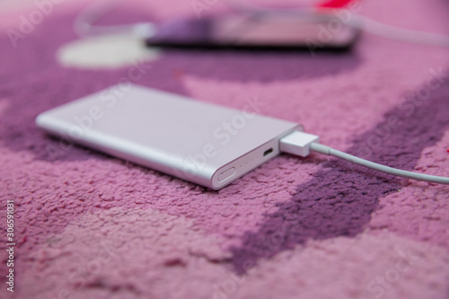 Smartphone Charging with silver Power Bank Through Spiral USB Cable . Smartphone charging with power bank on pink carpet . Energy bank .