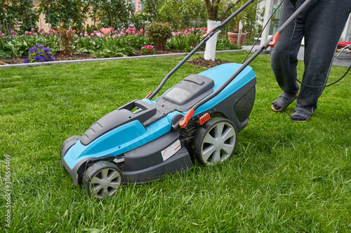 A man mows the lawn in his garden with an electric mower, close-up