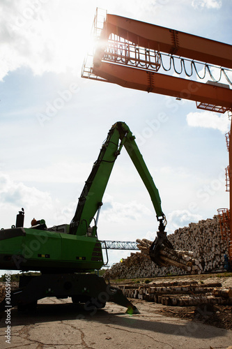 A reloader (excavator) and a gantry crane on the territory of an open log warehouse for a plywood factory