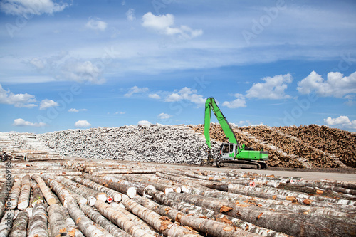 A reloader (excavator) in the open warehouse of logs for a plywood factory