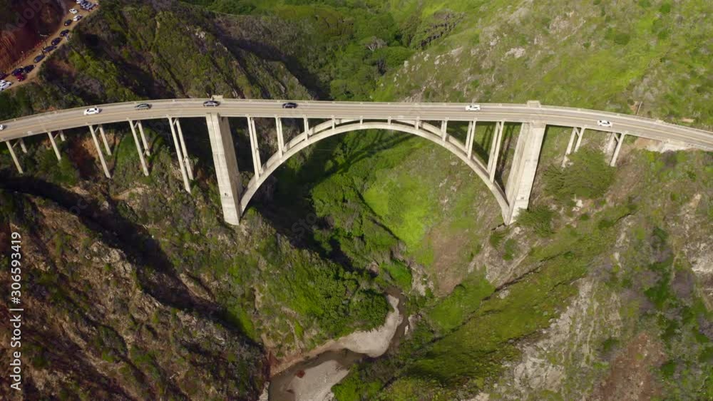 Aerial view of the picturesque arch bridge standing over the canyon among the beautiful hills covered with green grass. Cars move across the bridge. Famous landmark of USA under the cloudy sky. 4K Aerial view of the picturesque arch bridge standing over the canyon among the beautiful hills covered with green grass. Cars move across the bridge. Famous landmark of USA under the cloudy sky. 4K