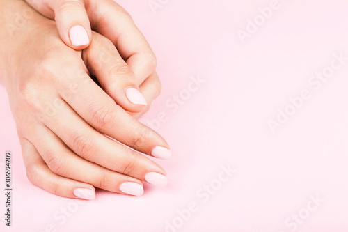 Female s hands with classic pastel manicure on pink background. Beauty salon.