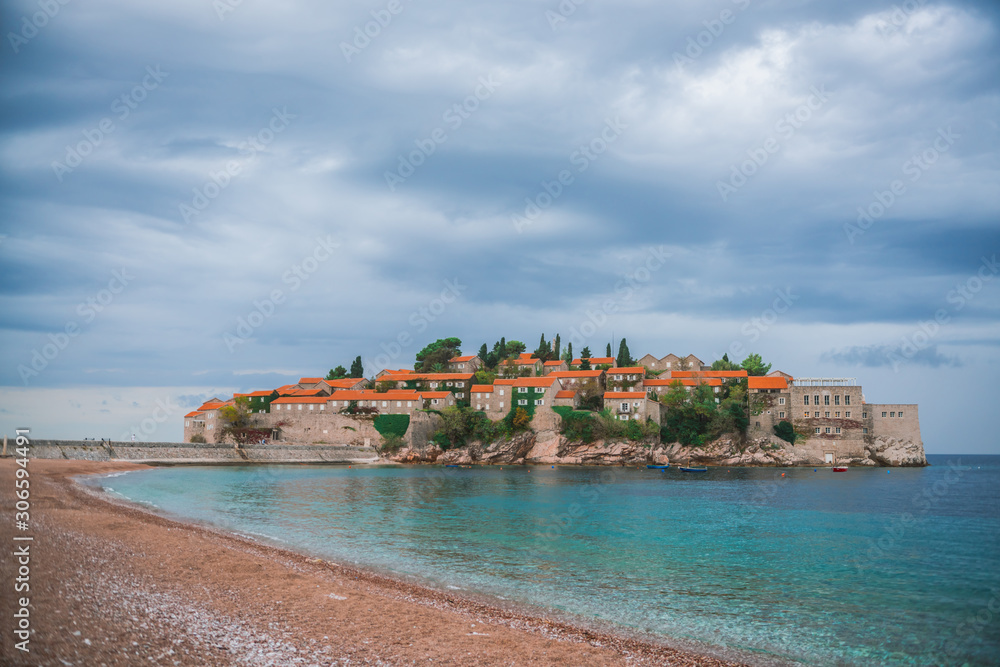 Sveti Stefan island in Montenegro. Mediterranean fortress on the island. Empty beach houses, with red roofs, the purest azure Adriatic sea.