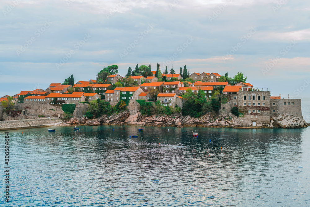 Sveti Stefan island in Montenegro. Small boats are moored off the island. Mediterranean fortress. Houses with red roofs, the ancient wall of the fortress.