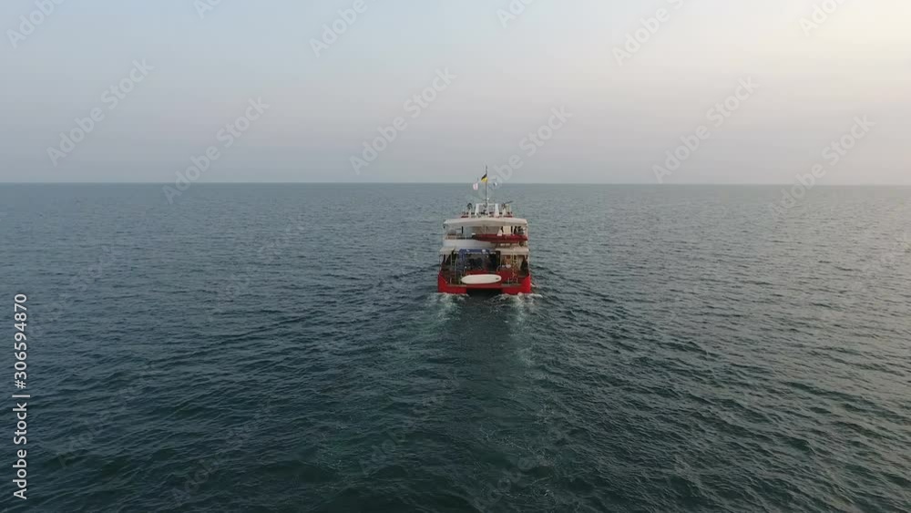 Aerial View from drone. Red catamaran, manned oceanographic explore vessel, is in full swing among open sea/ocean Aerial View from drone. Red catamaran, manned oceanographic explore vessel, is in full swing among open sea/ocean
