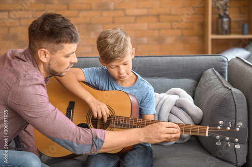 Father teaching his little son to play guitar at home photo