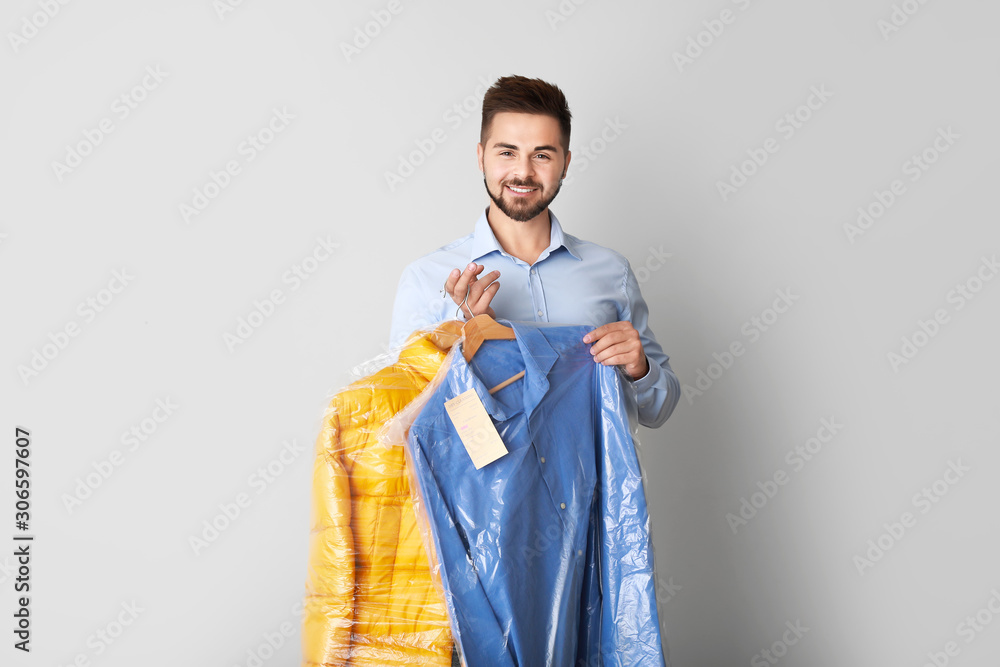 Male worker of modern dry-cleaner with clothes on light background Male worker of modern dry-cleaner with clothes on light background
