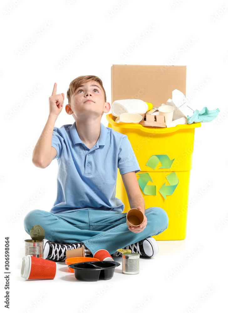 Little boy pointing at something while sitting near container with trash on white background. Concept of recycling Little boy pointing at something while sitting near container with trash on white background. Concept of recycling