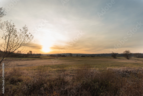 Rural landscape in Lublin Upland near Zamosc, dramatic view of sunset, colorful sky at fall evening, autumn fields and meadows, houses and roe deers in distant
