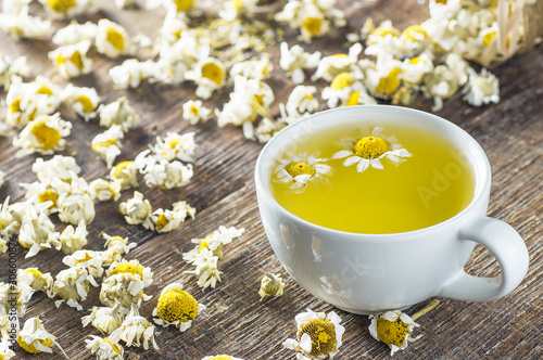 white cup of chamomile tea with dry daisy flowers on rustic wooden background  herbal medicine hot drink concept