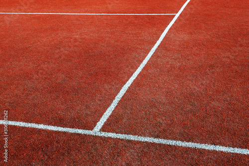 Part of empty used red tennis court playground surface with white lines closeup