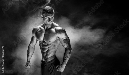 Bodybuilder posing. Fitness tattooed muscled man on smoke background. Studio shot.
