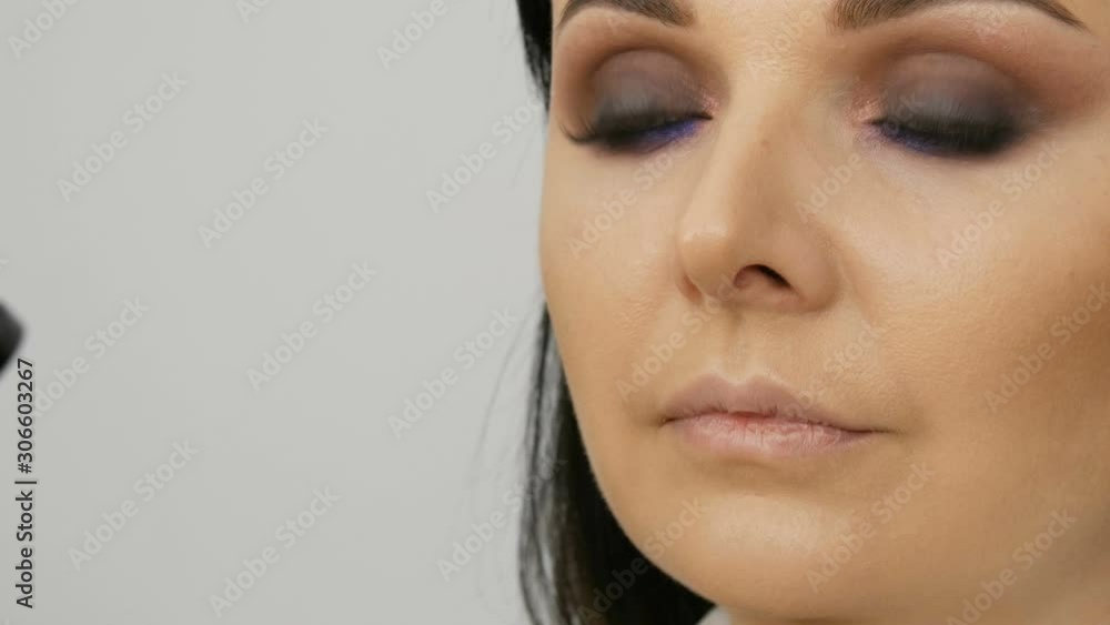 Stylist makeup artist applies foundation for face with a special brush on the face of a young beautiful woman with blue eyes Stylist makeup artist applies foundation for face with a special brush on the face of a young beautiful woman with blue eyes