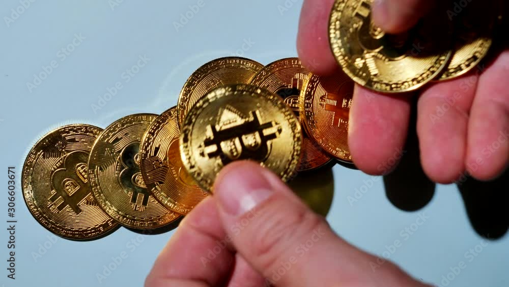 A hand distributes bitcoin coins on a blue surface.
