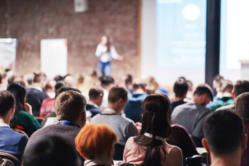 Adult people at conference listen to woman speaker providing lecture on scene in big conference hall. Business and Entrepreneurship concept. Audience at the conference hall.