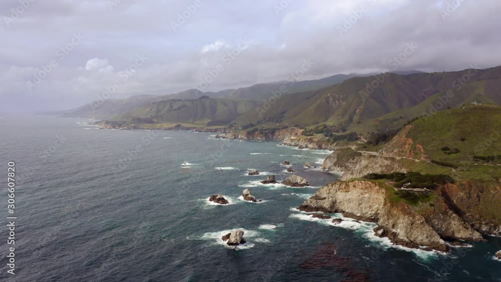The cloudy sky over the amazing landscape of Pacific Ocean coastline with rocky shore, green grassy mountains stretching to the horizon and calm ocean surface. Beautiful and majestic nature. Aerial,4K The cloudy sky over the amazing landscape of Pacific Ocean coastline with rocky shore, green grassy mountains stretching to the horizon and calm ocean surface. Beautiful and majestic nature. Aerial,4K