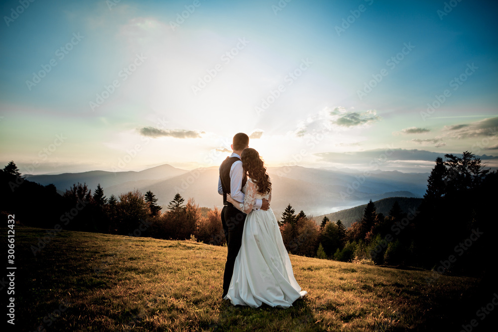 Bride and groom watch the sunset standing on the hill