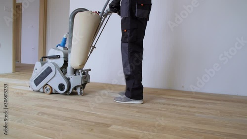 Scraping hardwood floor with the grinding machine. Repair in the apartment. Carpenter doing parquet wood floor polishing maintenance work by grinding machine