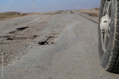 Close-up of a car wheel on a rural road near damaged asphalt, potholes. Concept rural road in poor condition