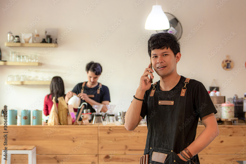 young asian barista in apron is using a smartphone, taking call with cell phone young asian barista in apron is using a smartphone, taking call with cell phone