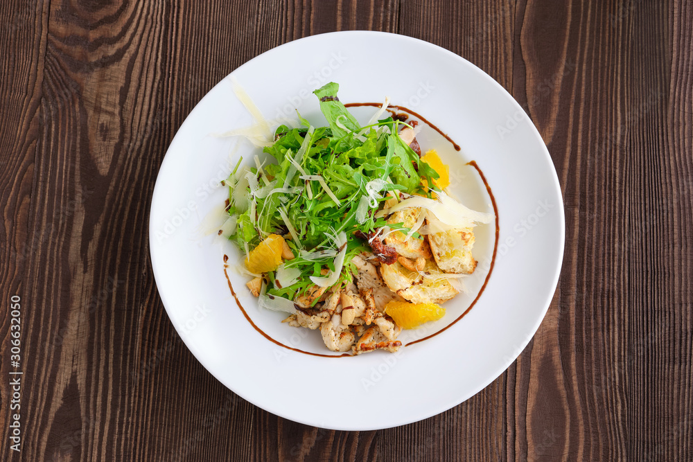 Top view of salad with fried chicken meat, dried tomato, cashew nuts and orange balsamic sauce served with arugula and parmesan on dark wooden background