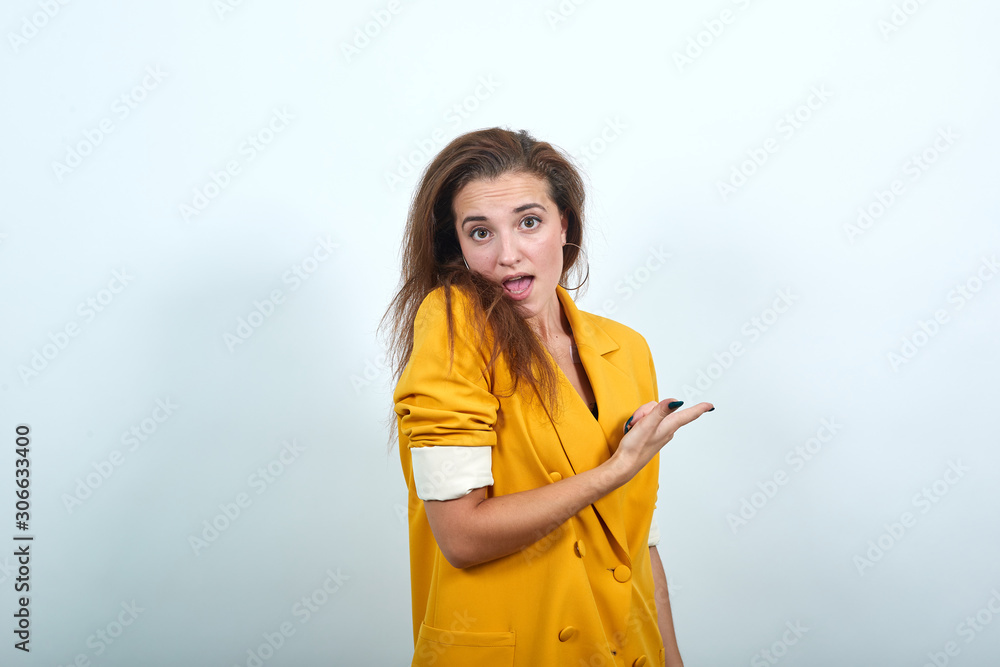 Shocked woman pointing aside, looking directly isolated on gray background in studio in yellow jacket. People sincere emotions, lifestyle concept. Shocked woman pointing aside, looking directly isolated on gray background in studio in yellow jacket. People sincere emotions, lifestyle concept.