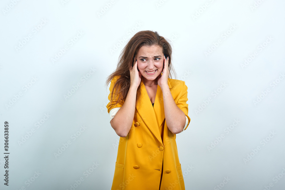 Attractive young woman in yellow jacket keeping hand on ears, headache isolated on gray background in studio. People sincere emotions, lifestyle concept. Attractive young woman in yellow jacket keeping hand on ears, headache isolated on gray background in studio. People sincere emotions, lifestyle concept.