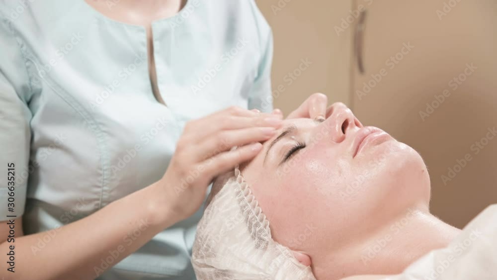 Girl beautician in a mask and gloves makes a salubrious facial massage to an attractive woman. New generation cosmetology massage Girl beautician in a mask and gloves makes a salubrious facial massage to an attractive woman. New generation cosmetology massage
