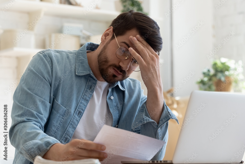 Upset frustrated young man holding reading postal mail letter Upset frustrated young man holding reading postal mail letter
