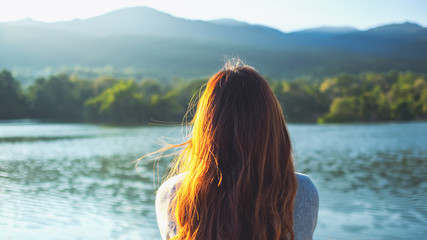 A woman sitting alone by the lake looking at the mountains with green nature background