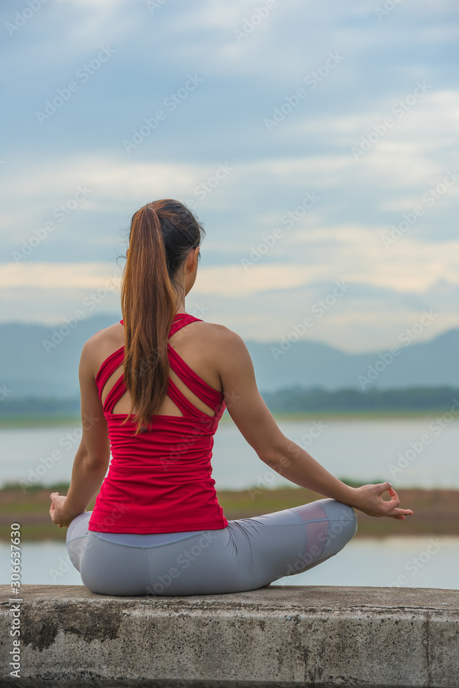 Yoga woman doing yoga pose on the wall at the lake with mountain background.