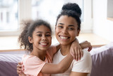 Portrait of smiling biracial mom and daughter cuddling at home