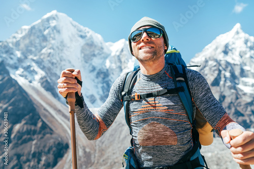 Fototapeta Naklejka Na Ścianę i Meble -  Portrait of smiling Hiker man on Taboche 6495m and Cholatse 6440m peaks background with trekking poles, UV protecting sunglasses. He enjoying mountain views during Everest Base Camp trekking route.