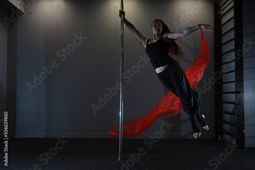 The dancer on the pylon in the studio. Girl doing exercises on a sports equipment. © alexkich