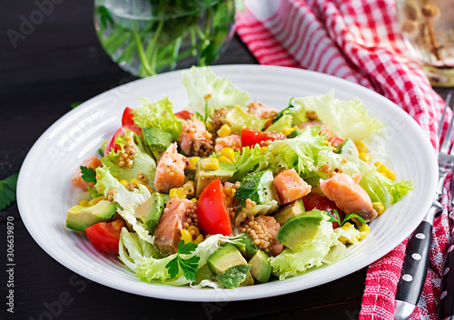 Salad with grilled salmon, lettuce, avocado, tomatoes and corn on a white bowl. Paleo diet.