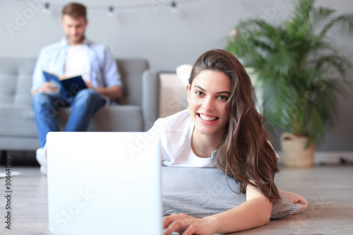 Smiling beautiful woman using laptop with blurred man in background at home.