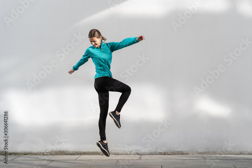 Young adult sporty woman jumping up against wall outdoor