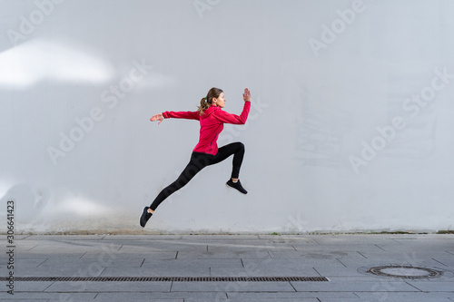 Young adult athletic woman jumping up against wall outdoor