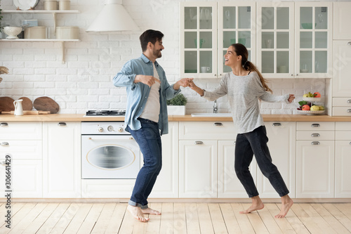 Happy active young couple husband and wife dancing in kitchen