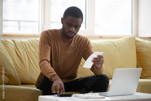Concentrated biracial man calculating household expenses at home photo