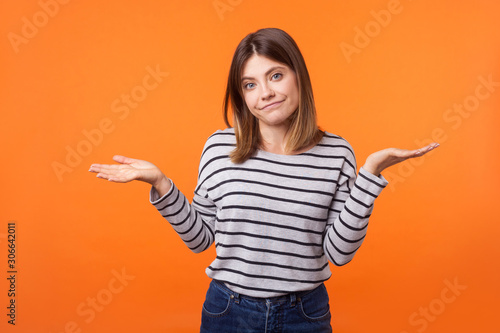 Don't know! Portrait of uncertain confused brunette woman in long sleeve shirt standing having doubts while raised hands, clueless facial expression. indoor studio shot isolated on orange background