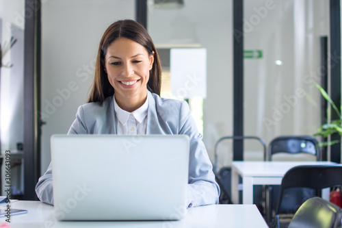 Beautiful young businesswoman in formal wear using laptop in office