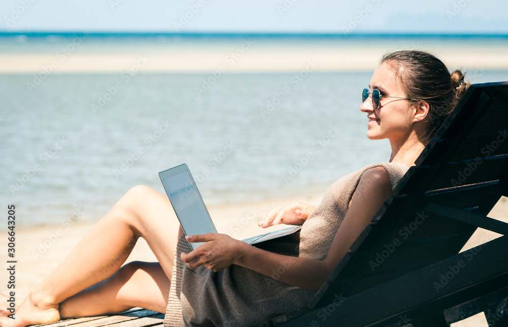 Young beautiful girl communicates remotely using laptop on beach